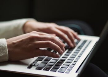 Hands typing on a laptop keyboard in a dimly lit setting.