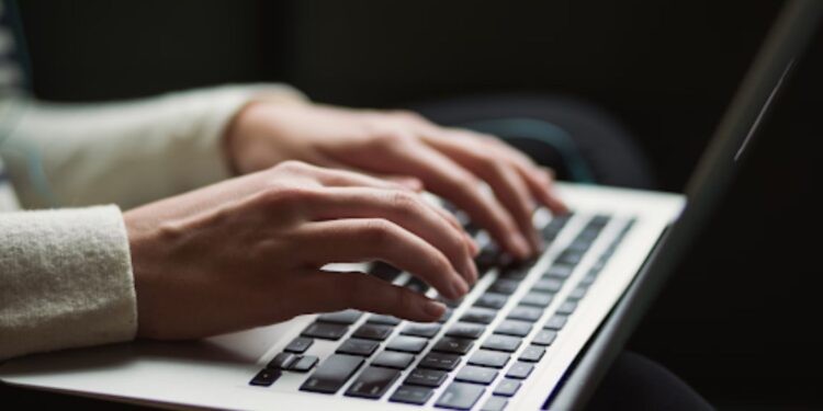Hands typing on a laptop keyboard in a dimly lit setting.